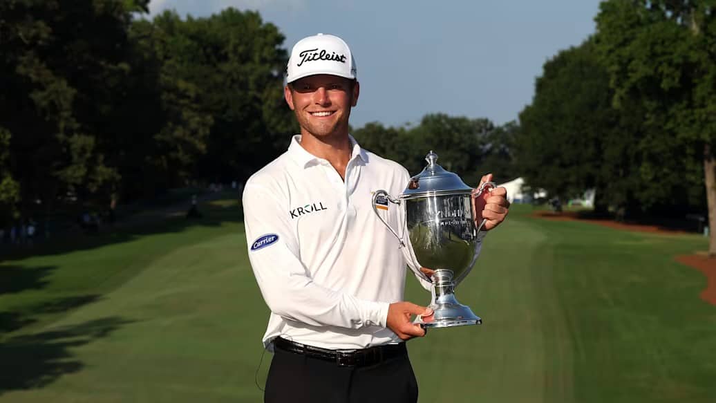 The tournament champion holding the trophy on the course at sunset